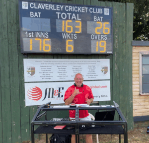 A man stands smiling underneath an electronic cricket scoreboard.