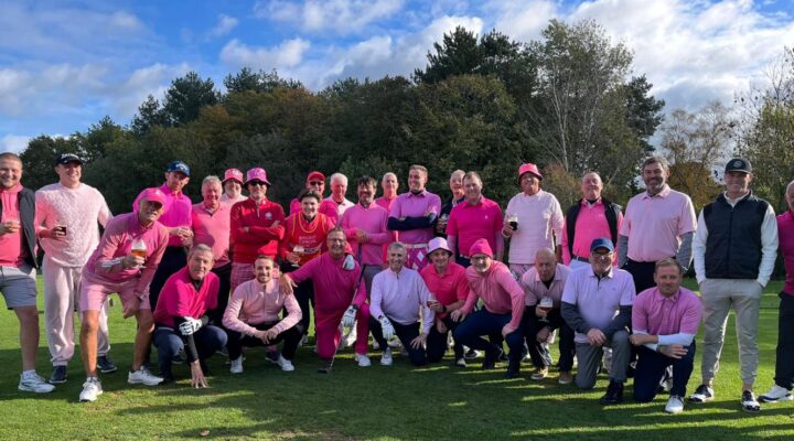 A group of men wearing pink pose for the camera on the golf course.
