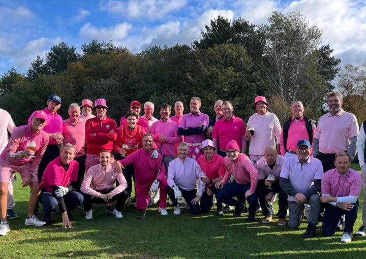 A group of men wearing pink pose for the camera on the golf course.