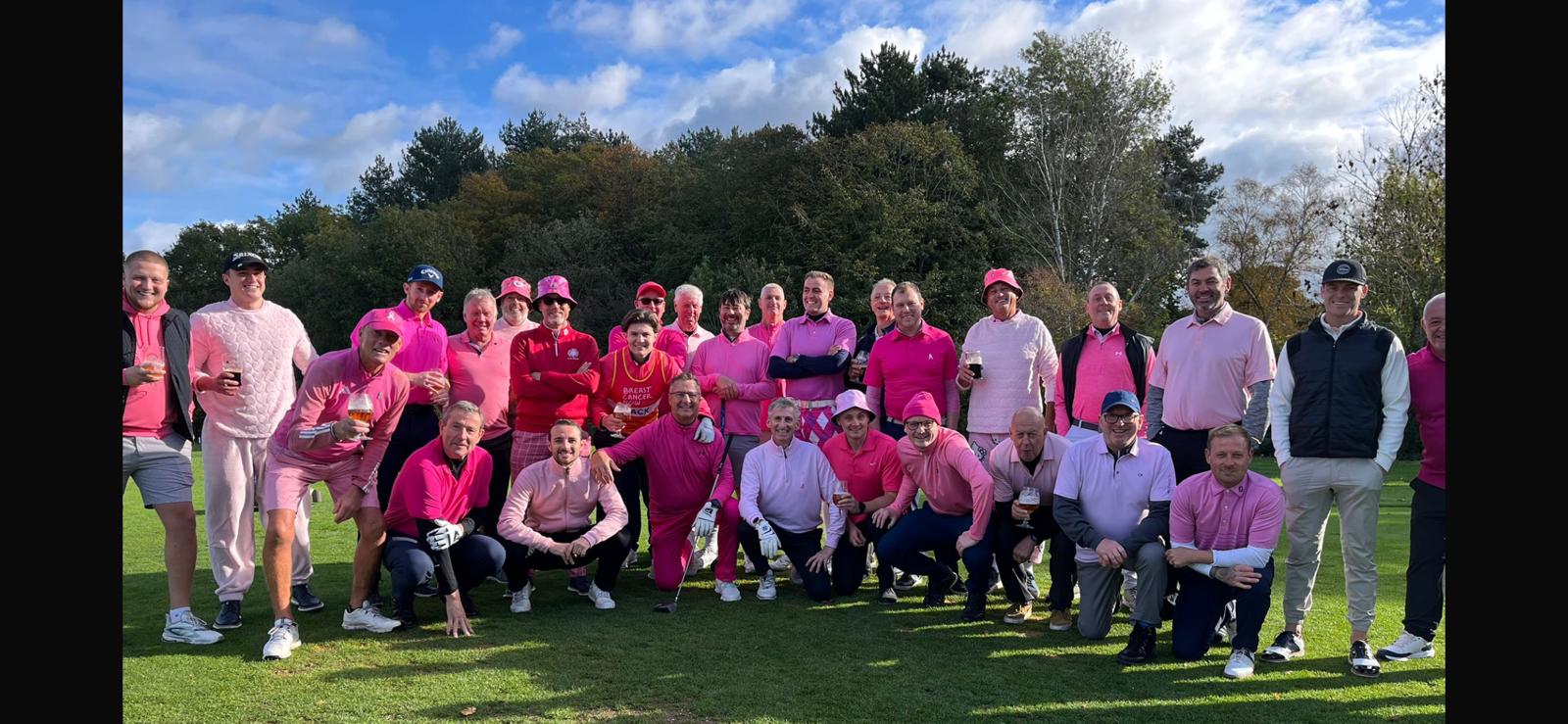 A group of men wearing pink pose for the camera on the golf course.