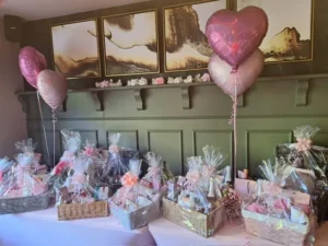 A table of pink themed hampers decorated with four pink metallic helium balloons in the shape of hearts.