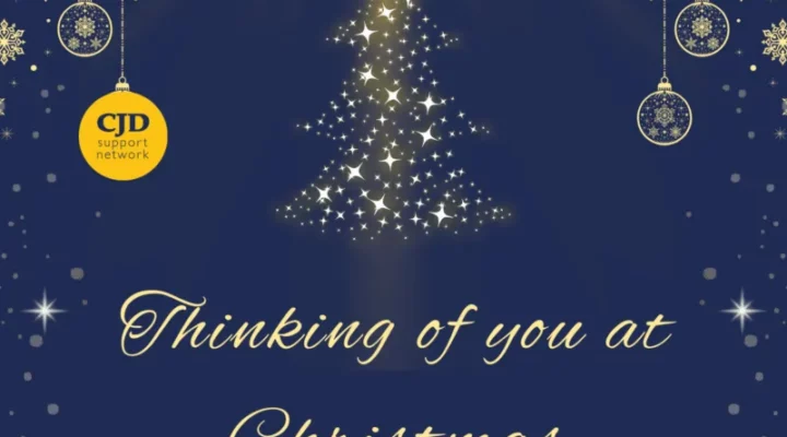 A christmas card with a navy background. It says 'Thinking of you at Christmas' and shows a Christmas Tree shape made out of sparkles. There are delicate baubles hanging from the top of the card. One of them is the CJD Support Network logo. At the base of the card it says 'Supporting the CJD Support Network'.