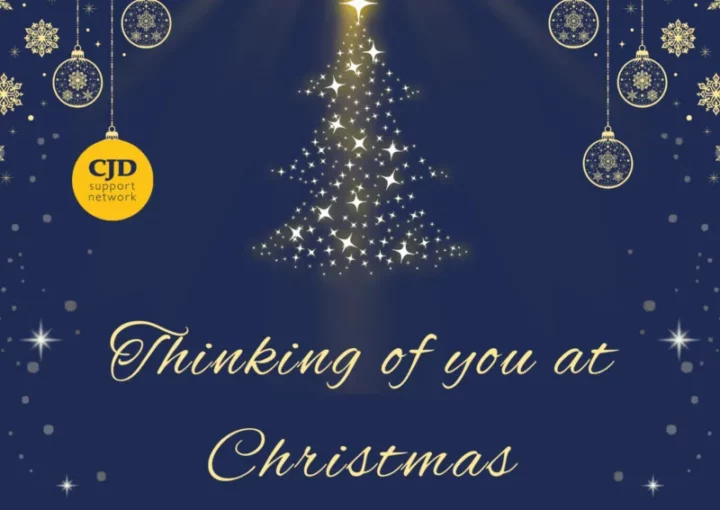 A christmas card with a navy background. It says 'Thinking of you at Christmas' and shows a Christmas Tree shape made out of sparkles. There are delicate baubles hanging from the top of the card. One of them is the CJD Support Network logo. At the base of the card it says 'Supporting the CJD Support Network'.
