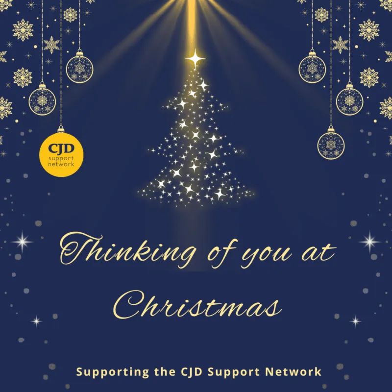 A christmas card with a navy background. It says 'Thinking of you at Christmas' and shows a Christmas Tree shape made out of sparkles. There are delicate baubles hanging from the top of the card. One of them is the CJD Support Network logo. At the base of the card it says 'Supporting the CJD Support Network'.