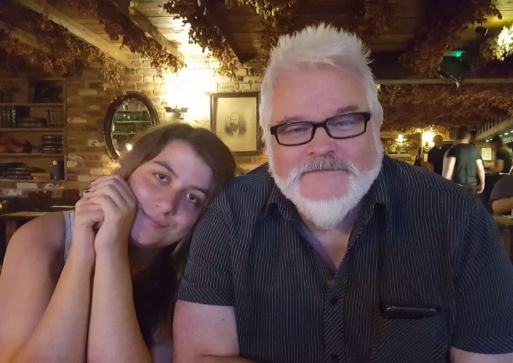 A photo taken in a pub. A young woman, Jodie, leans her head against the shoulder of a man with a white beard. This is her father, Taff. They look totally comfortable together.