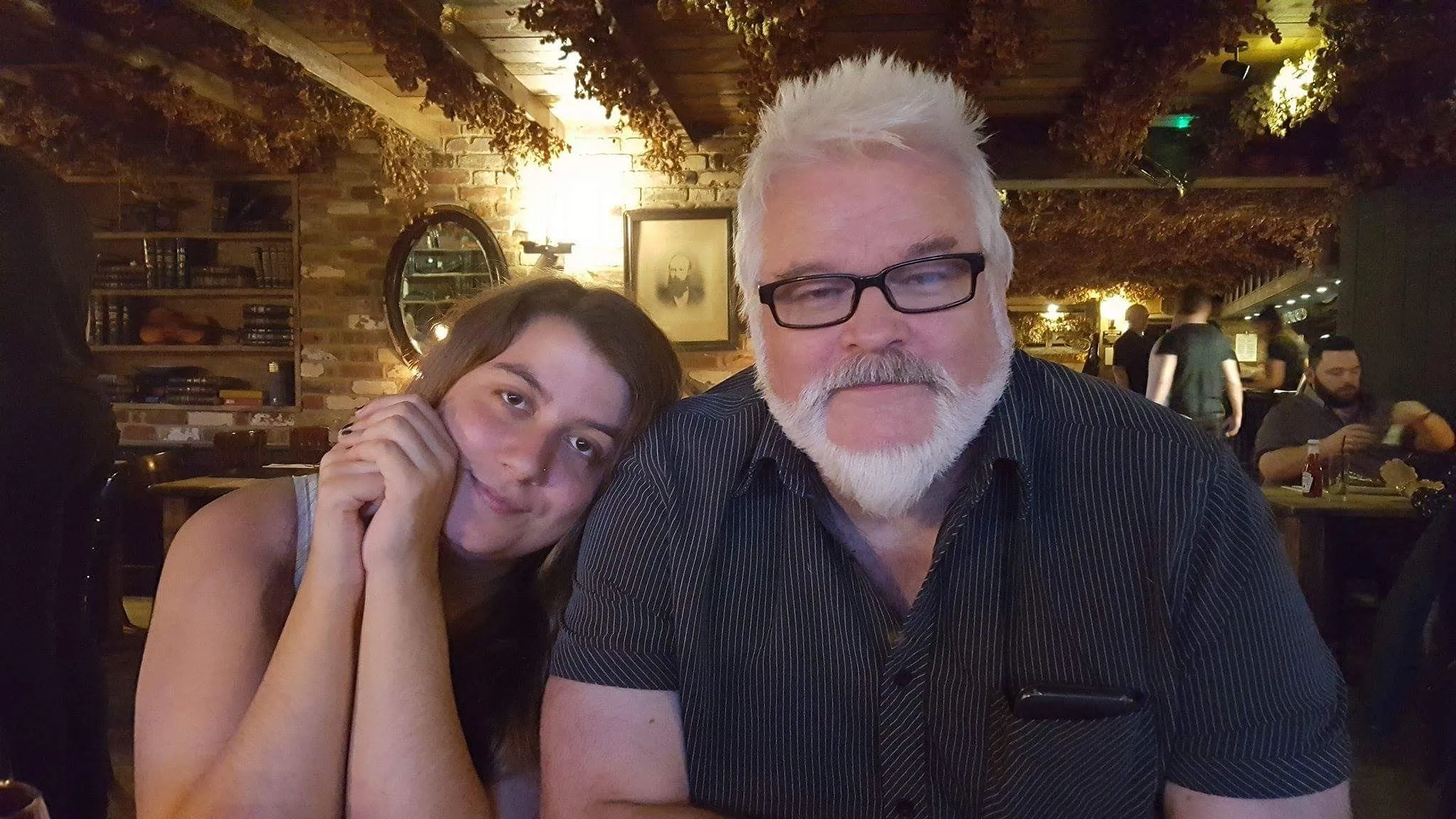 A photo taken in a pub. A young woman, Jodie, leans her head against the shoulder of a man with a white beard. This is her father, Taff. They look totally comfortable together.